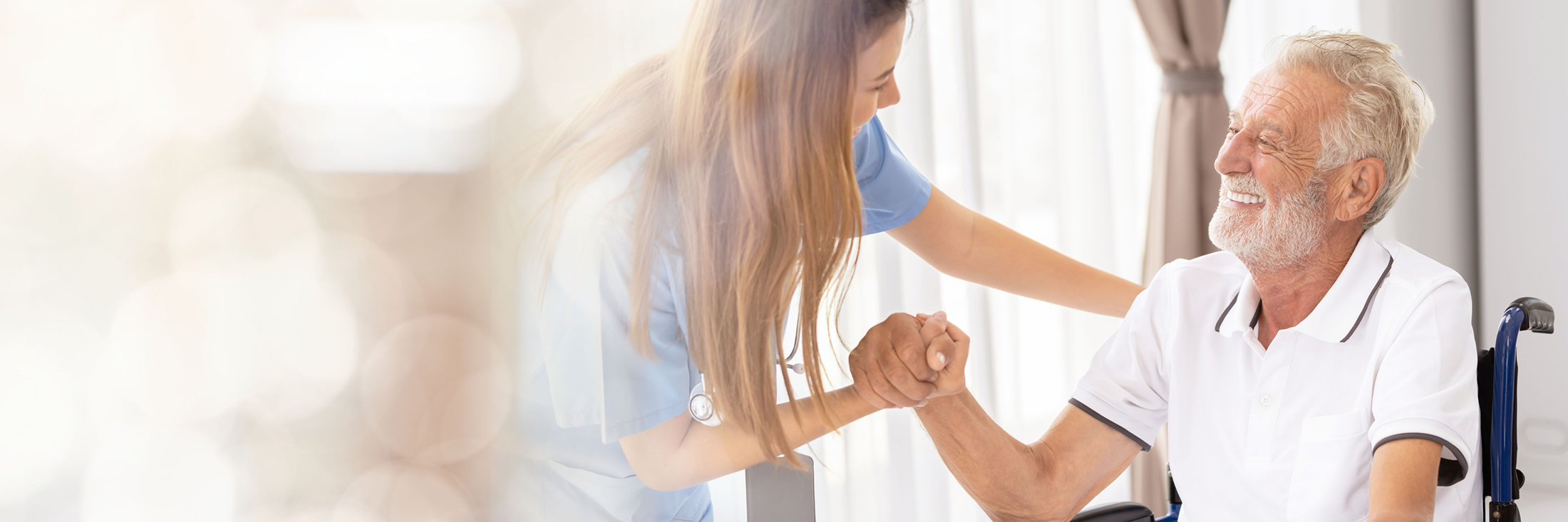 Female nurse shakes an older man's hand as he sits in a wheelchair smiling.